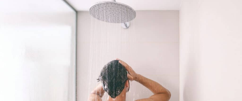 Homem de costas lavando o cabelo no chuveiro