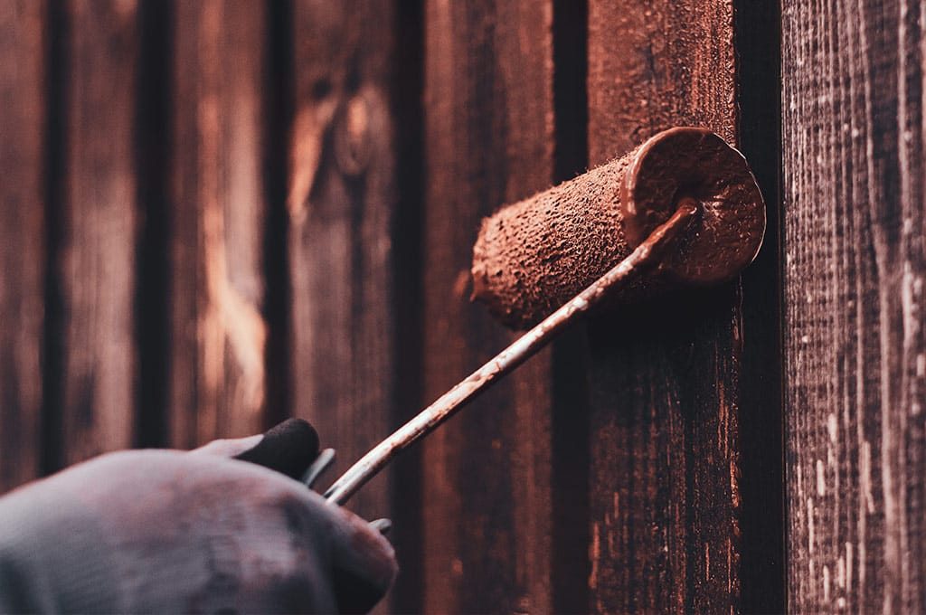 Mão com rolo pintando madeira