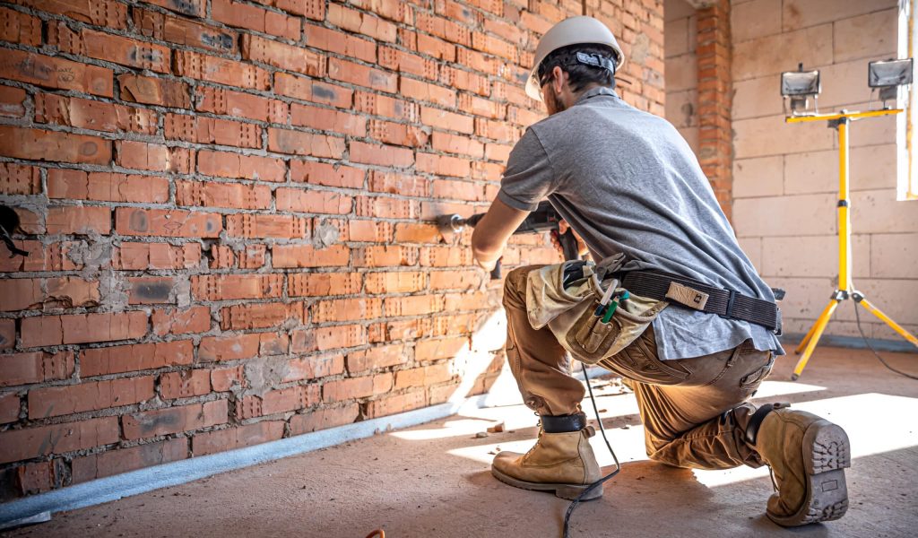 A builder works with a drill at a construction site. Tudo sobre acabamentos